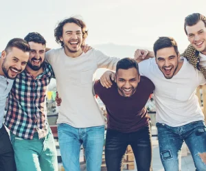 Groupe de jeunes hommes complices, bras autour des épaules, riant ensemble sur une terrasse urbaine en plein jour.